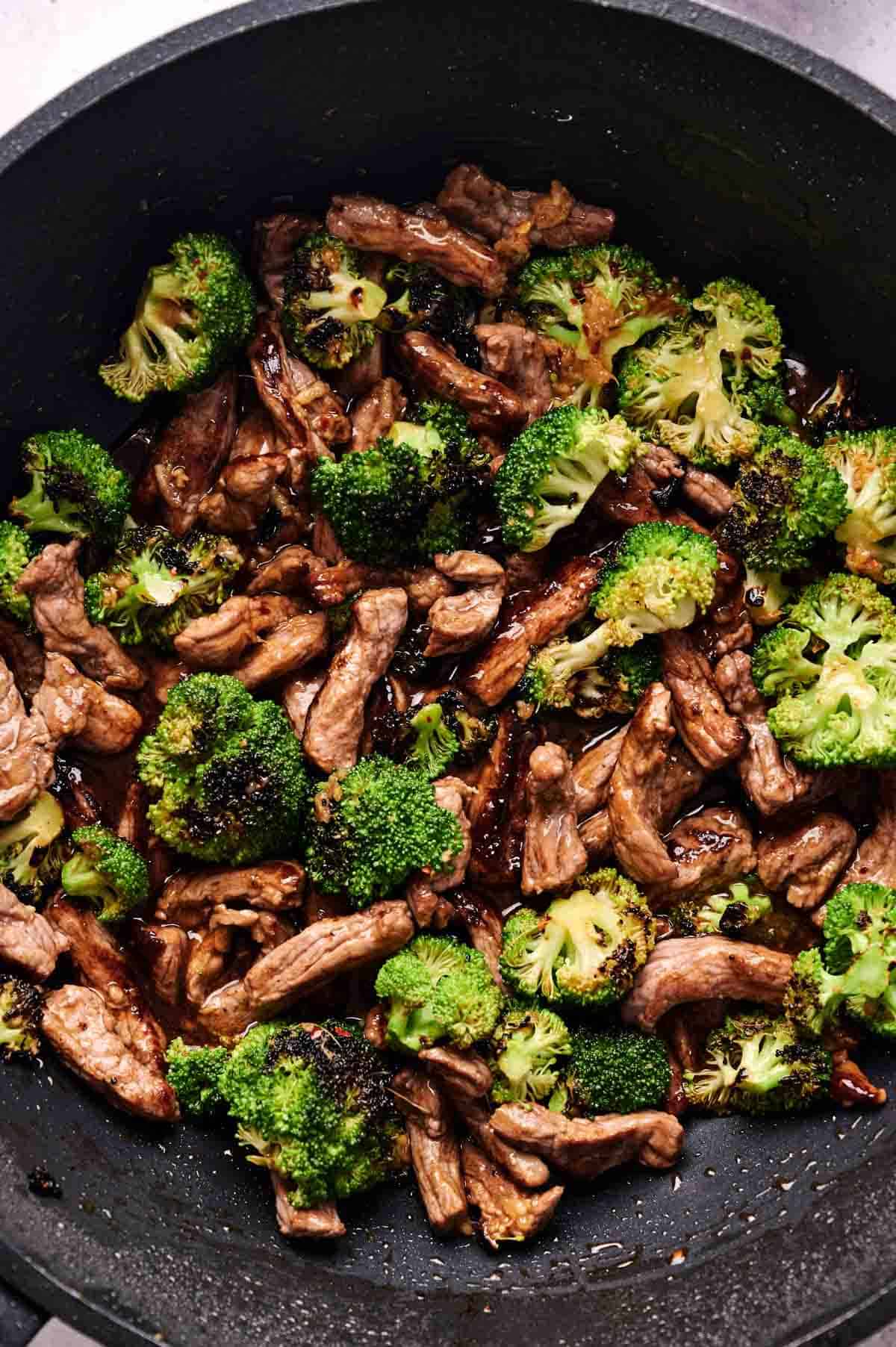 Tender beef and broccoli florets are cooked together in a black skillet for a classic Beef and Broccoli dish.
