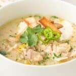 A bowl of creamy Slow Cooker White Chicken Chili garnished with cilantro, sliced green chili, tortilla strips, and a dollop of sour cream.