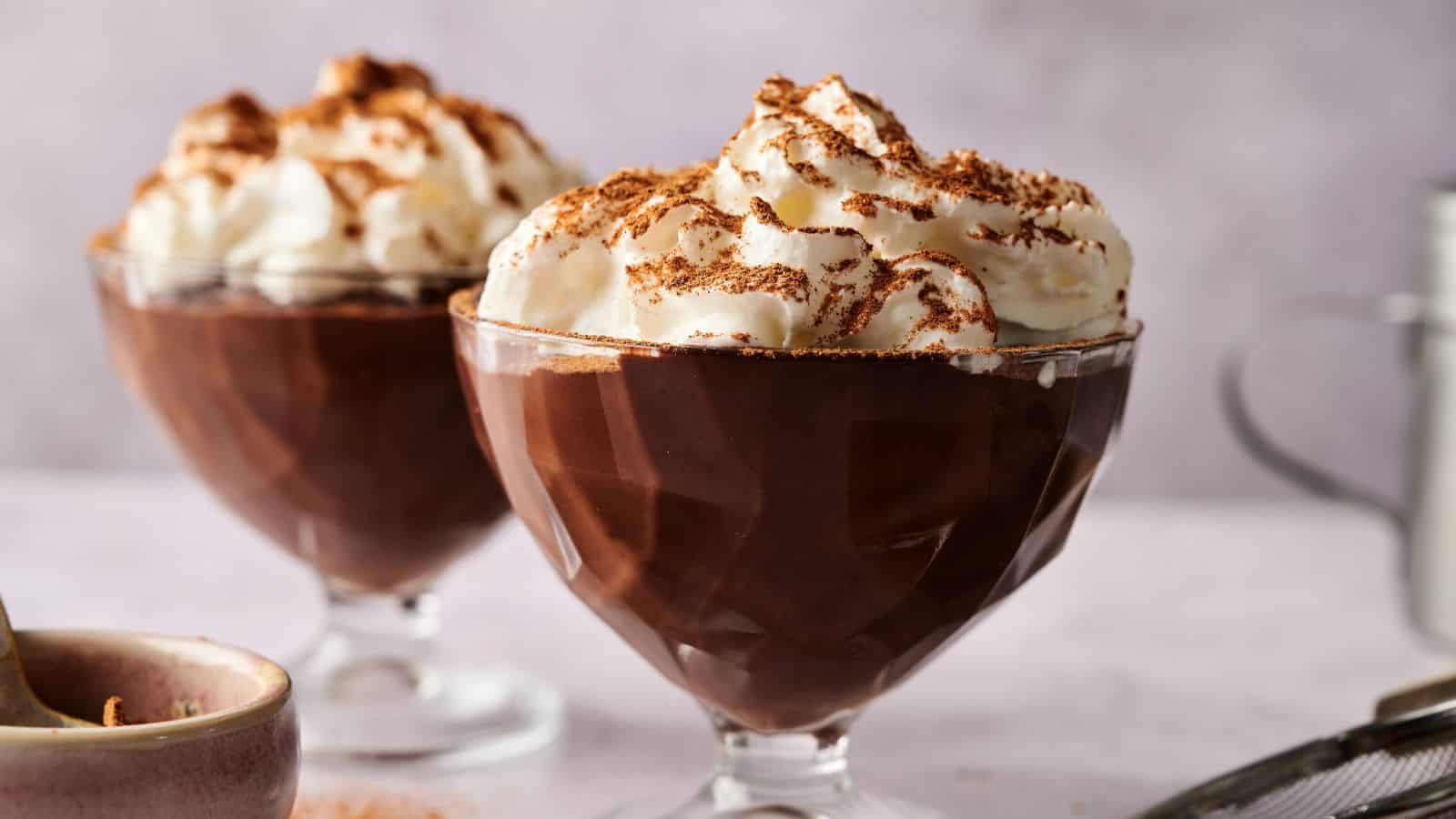 Two glass dessert cups filled with chocolate pudding, each topped with whipped cream and chocolate shavings.