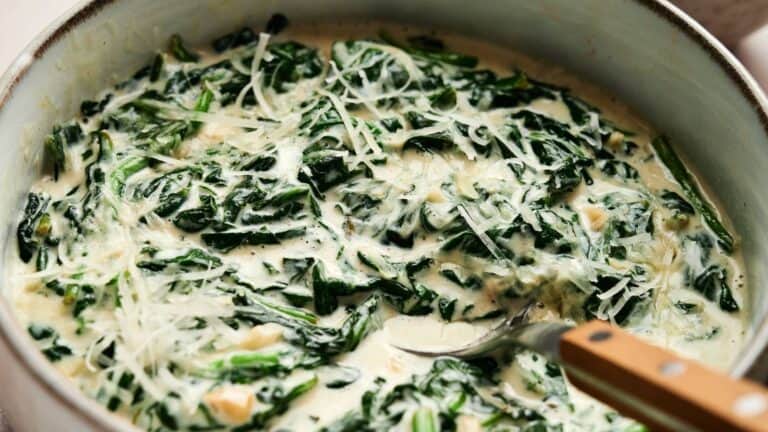 A bowl of creamy spinach topped with grated cheese, being stirred with a wooden-handled spoon.