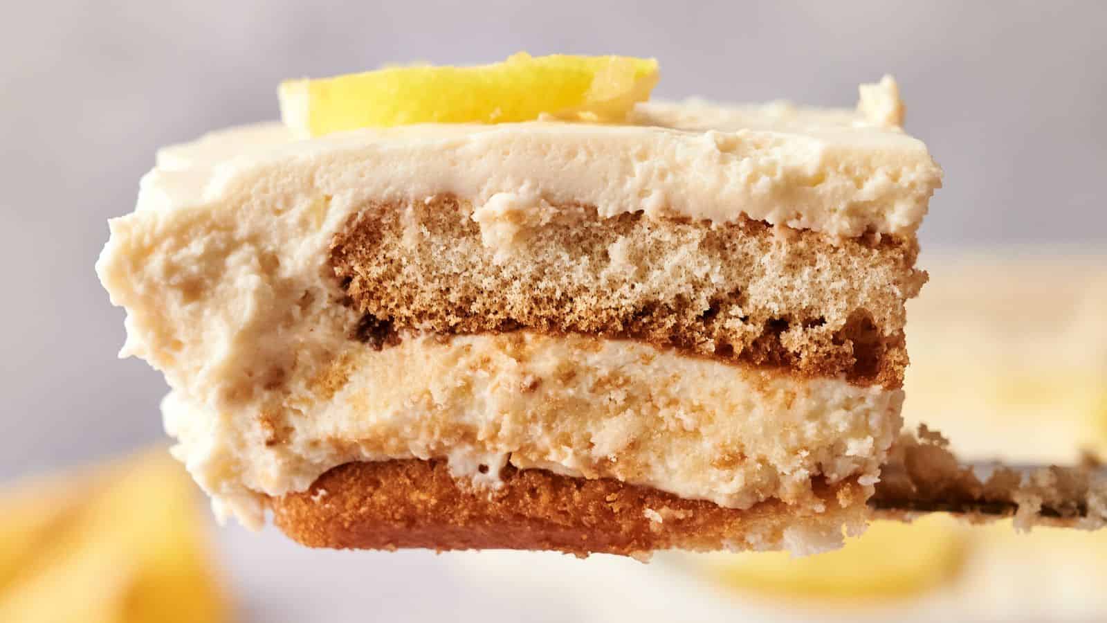 A close-up of a slice of layered tiramisu with cream, cake layers, and a lemon wedge garnish on top.