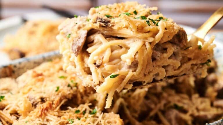 A close-up of a serving of baked spaghetti with a creamy sauce, mushrooms, and a golden breadcrumb topping, garnished with chopped herbs.