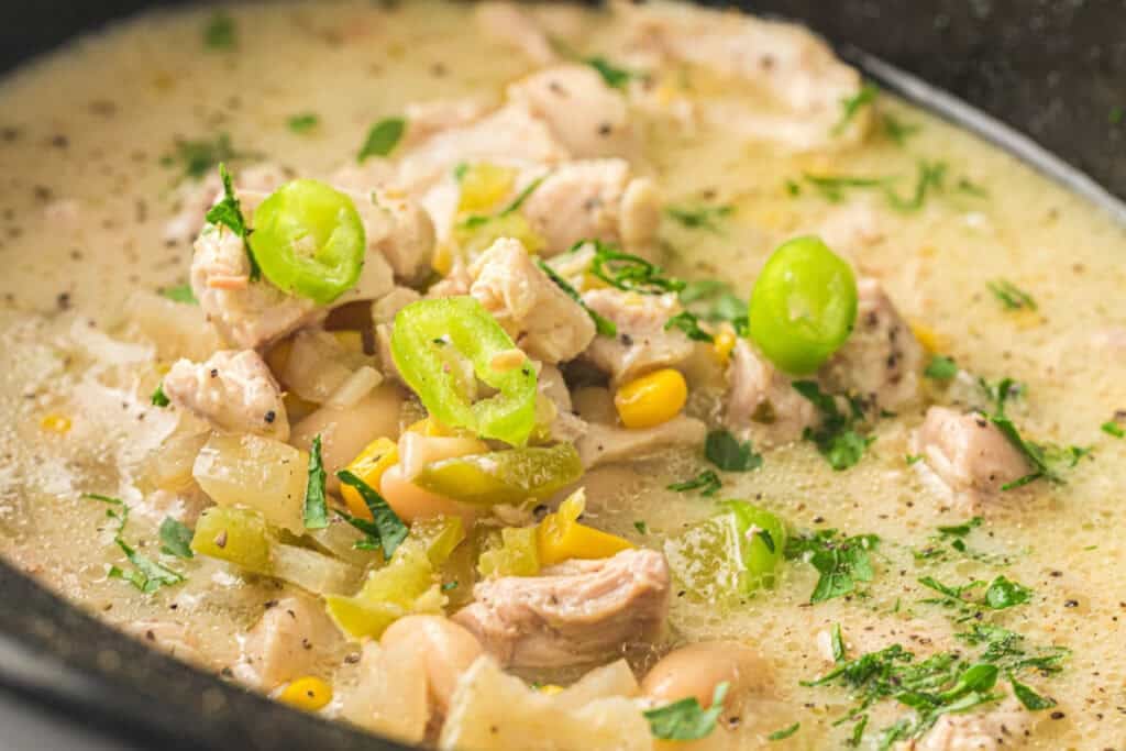 Close-up of a bowl of Slow Cooker White Chicken Chili with tender chicken, white beans, corn, green chilies, herbs, and a creamy broth.