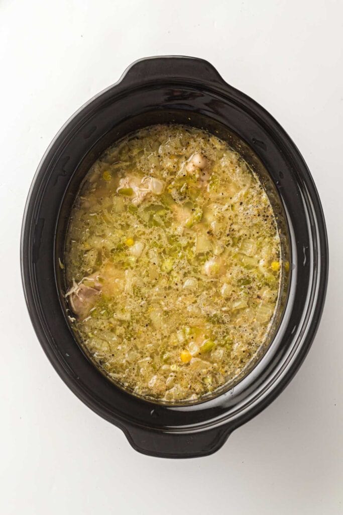 A slow cooker filled with Slow Cooker White Chicken Chili, brimming with tender chicken, vegetables, and herbs, viewed from above on a white background.