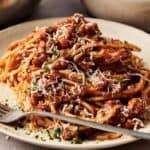 A plate of spaghetti topped with savory Turkey Bolognese sauce, garnished with grated cheese and parsley, with a fork resting on the plate.