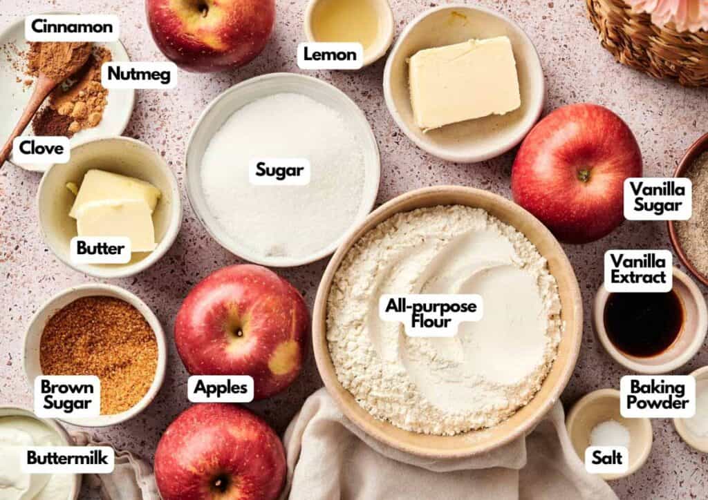 Top-down view of baking ingredients for Air Fryer Apple Cobbler, including apples, flour, sugars, butter, spices, lemon, buttermilk, and labeled items arranged on a light surface.