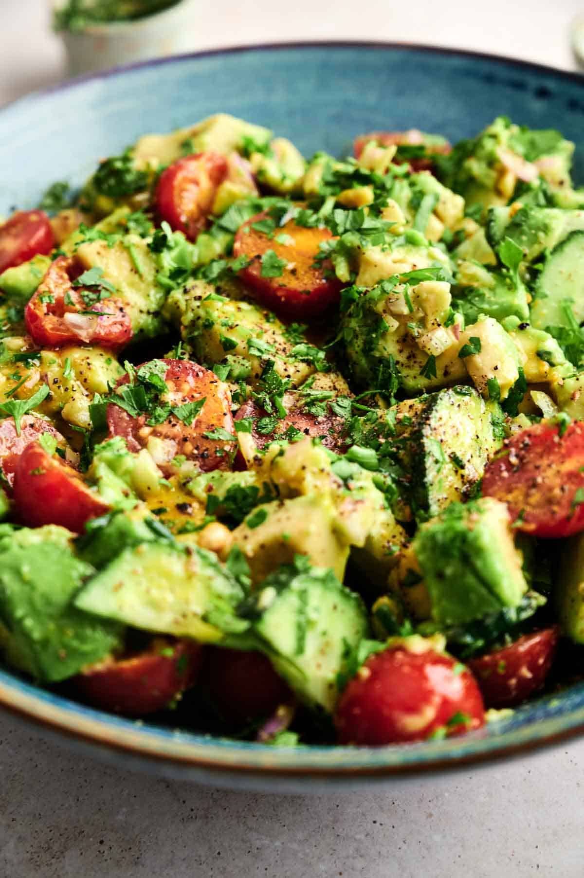 A close-up of a bowl filled with fresh Avocado Salad, featuring cherry tomato, cucumber, corn, and cilantro.