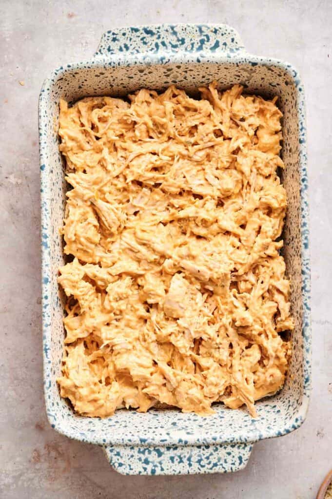 A speckled baking dish filled with an uncooked mixture of shredded chicken and creamy sauce for Buffalo Chicken Sliders, set on a light-colored surface.