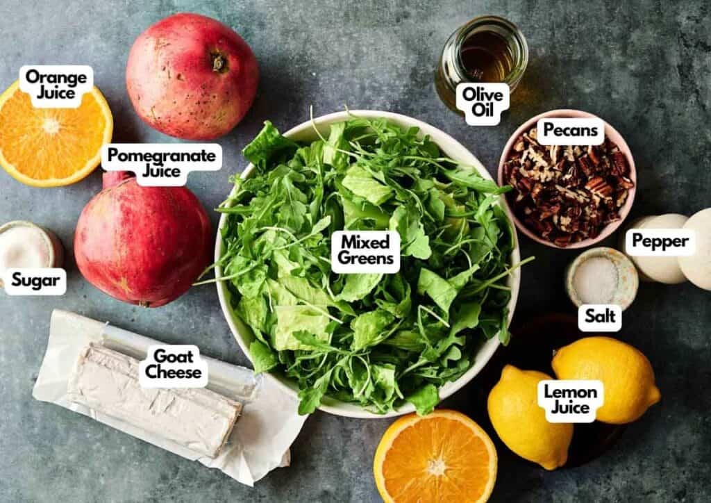 A festive Christmas Salad features a bowl of mixed greens surrounded by labeled ingredients: orange juice, pomegranate juice, sugar, goat cheese, pecans, olive oil, salt, pepper, and lemon juice.