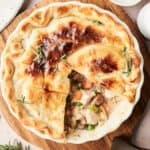 A baked Air Fryer Turkey Pot Pie with a golden crust, a slice removed to reveal turkey, peas, carrots, and celery filling, garnished with rosemary on a wooden board.