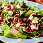 A close-up of a festive Christmas Salad with romaine lettuce, pecans, pomegranate seeds, and cubes of cheese on a blue plate.