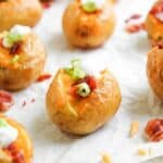 Loaded Baked Potato Bites: Mini baked potatoes topped with melted cheese, sour cream, bacon bits, and chopped green onions, all arranged on parchment paper for the perfect party snack.