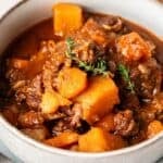 A bowl of Slow Cooker Beef Stew with chunks of beef, carrots, potatoes, and garnished with fresh thyme in a rich brown broth.