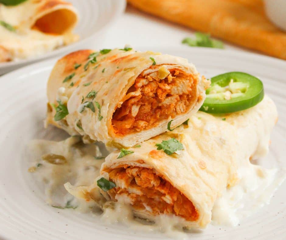 Two White Chicken Enchiladas topped with creamy white sauce, sliced jalape&ntilde;o, and chopped cilantro on a white plate.