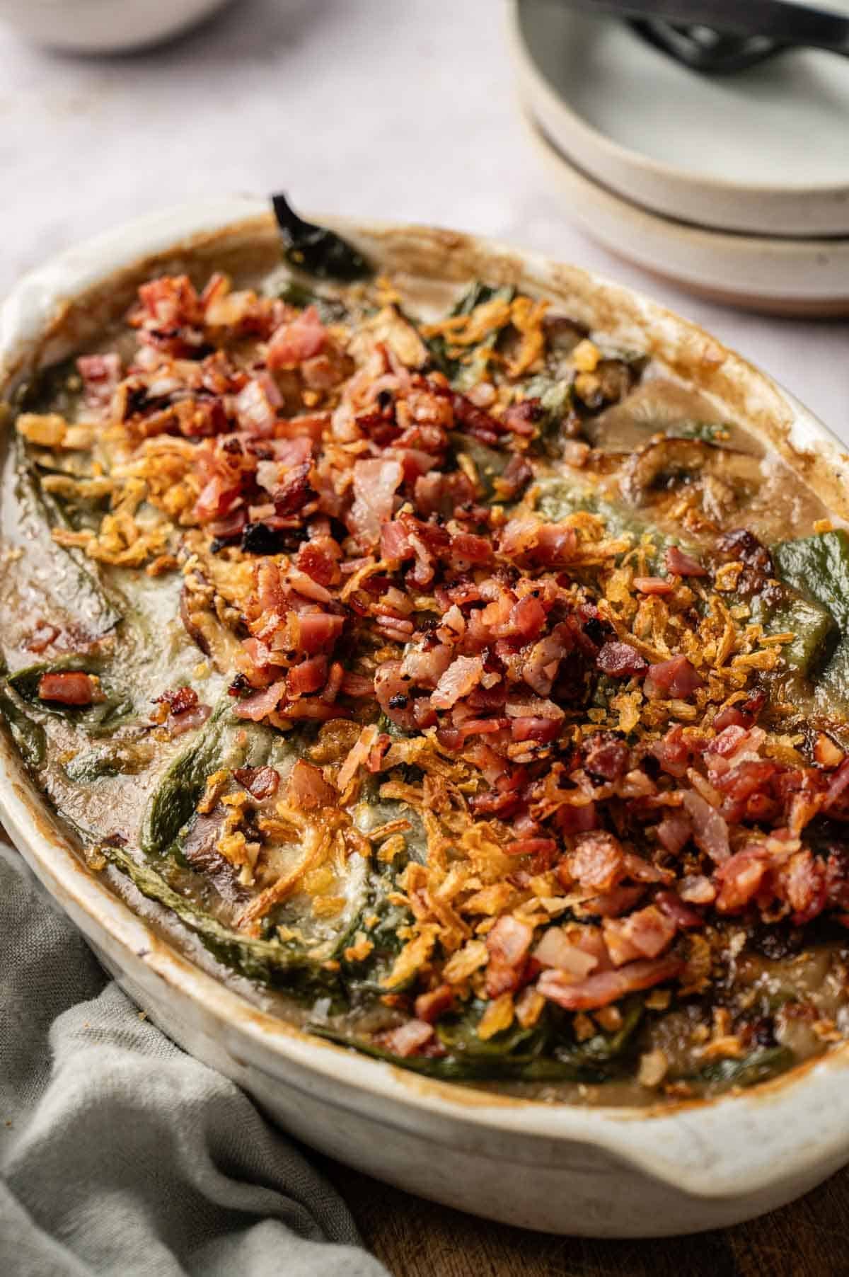 A casserole dish filled with a creamy Green Bean and Bacon Casserole, topped with crispy bacon pieces and fried onions.