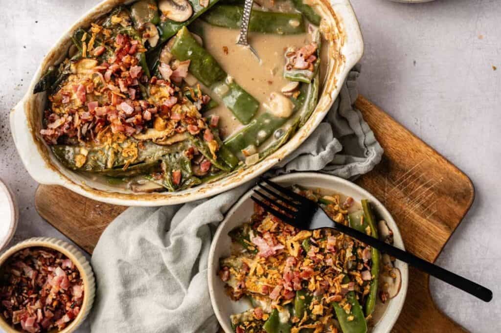 A Green Bean and Bacon Casserole with creamy green beans, mushrooms, and crispy bacon bits is served on a plate with a black fork.