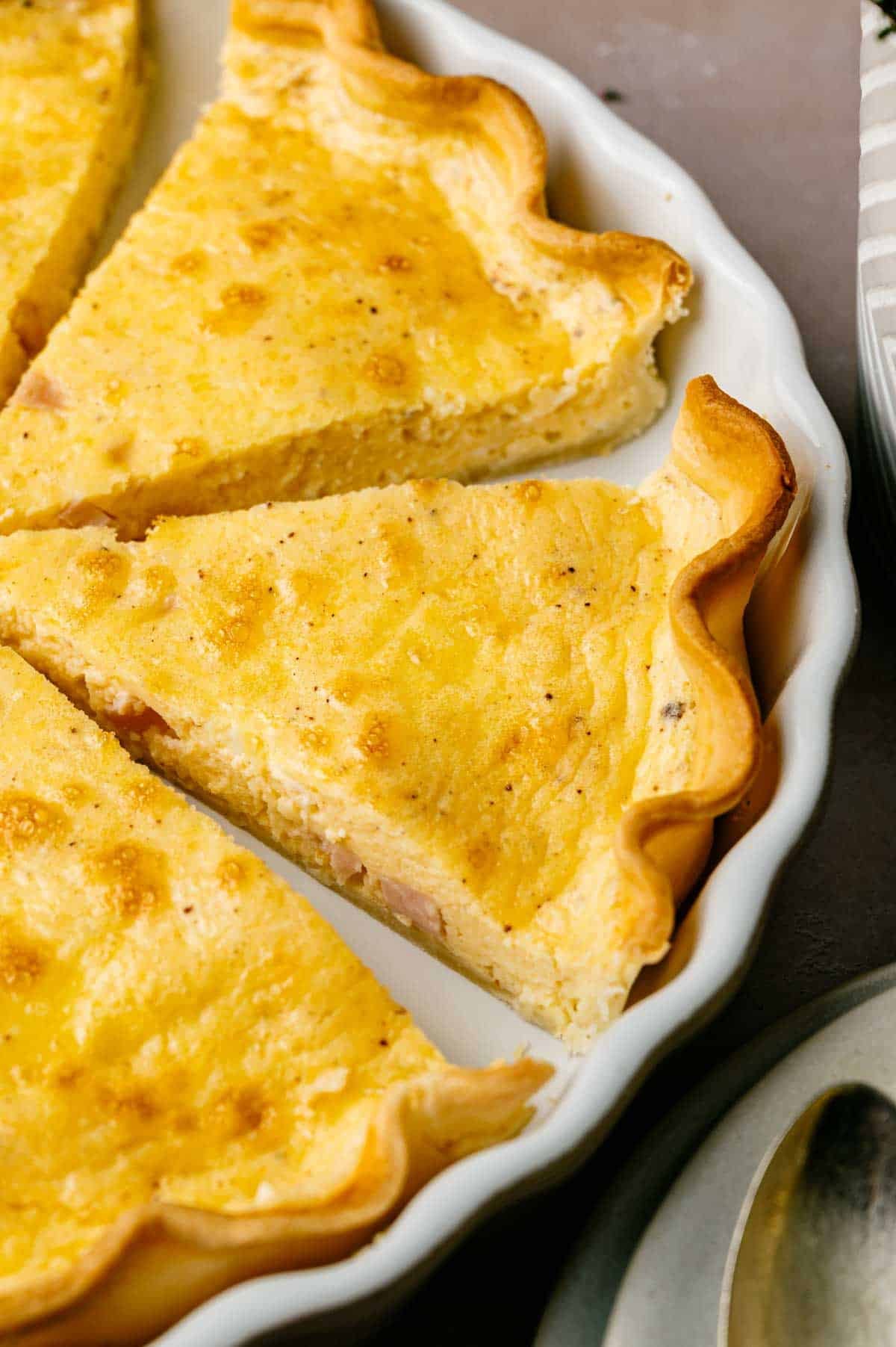Three slices of Ham and Cheese Quiche with a golden, flaky crust are arranged in a white ceramic pie dish.