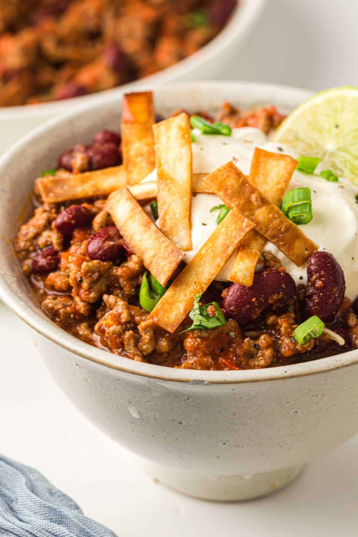 A bowl of Instant Pot Chili topped with sour cream, crispy tortilla strips, chopped green onions, and a lime wedge.