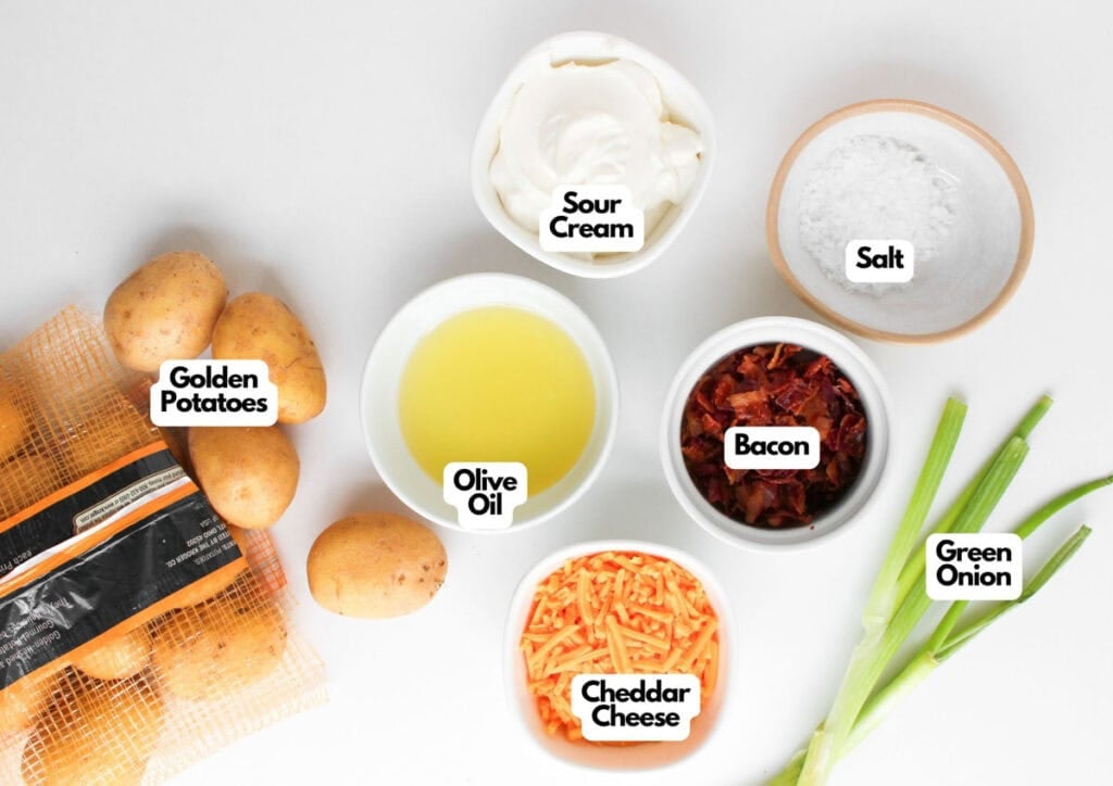 Various ingredients labeled on a white surface, including golden potatoes, olive oil, cheddar cheese, sour cream, salt, bacon, and green onion&mdash;everything you need to make irresistible Loaded Baked Potato Bites.