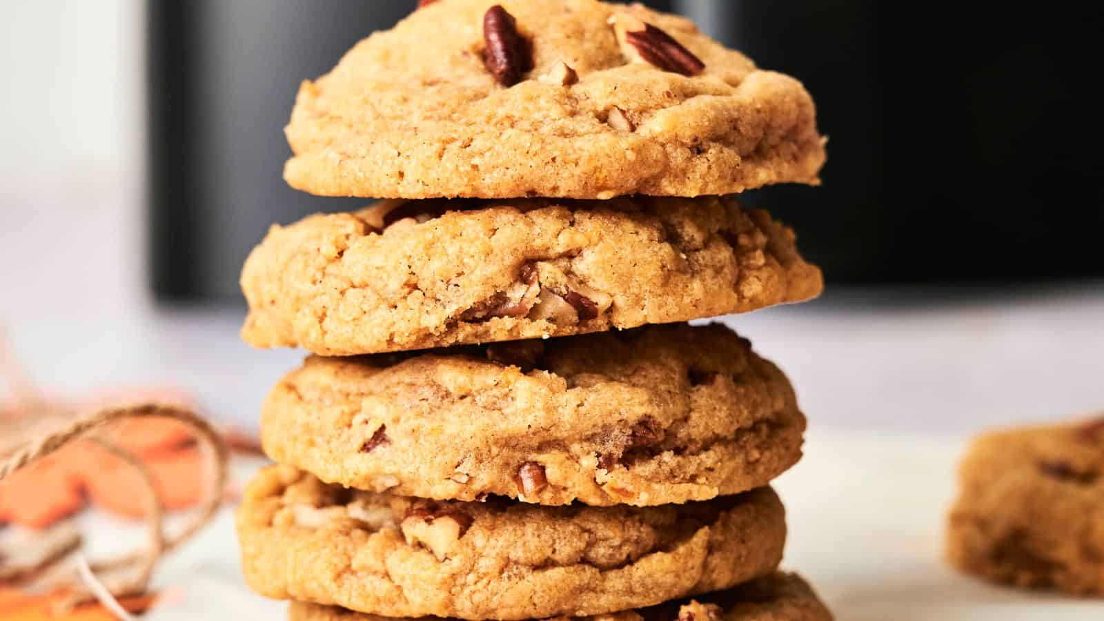A stack of four thick, golden brown cookies with visible nut pieces, placed on a light surface.