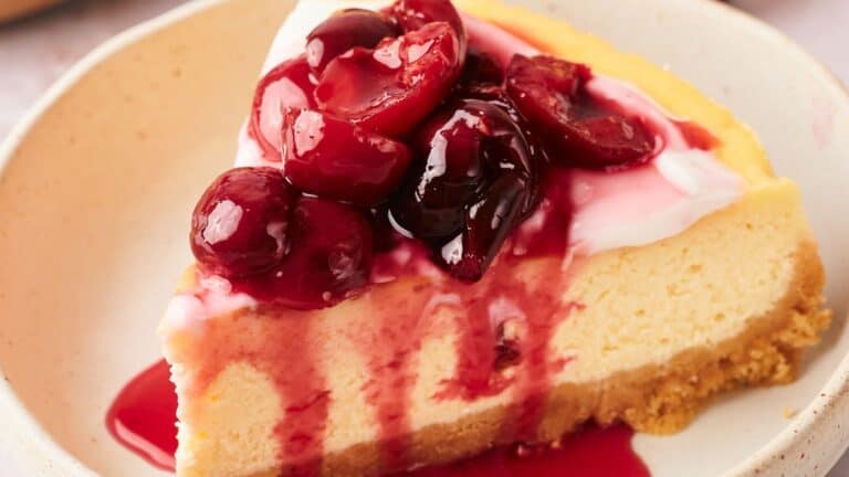 A slice of cheesecake topped with cherry sauce sits on a beige plate.