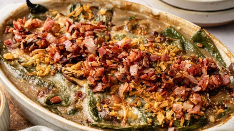 A baked casserole dish filled with stuffed green peppers, topped with melted cheese, crispy bacon, and fried onions.