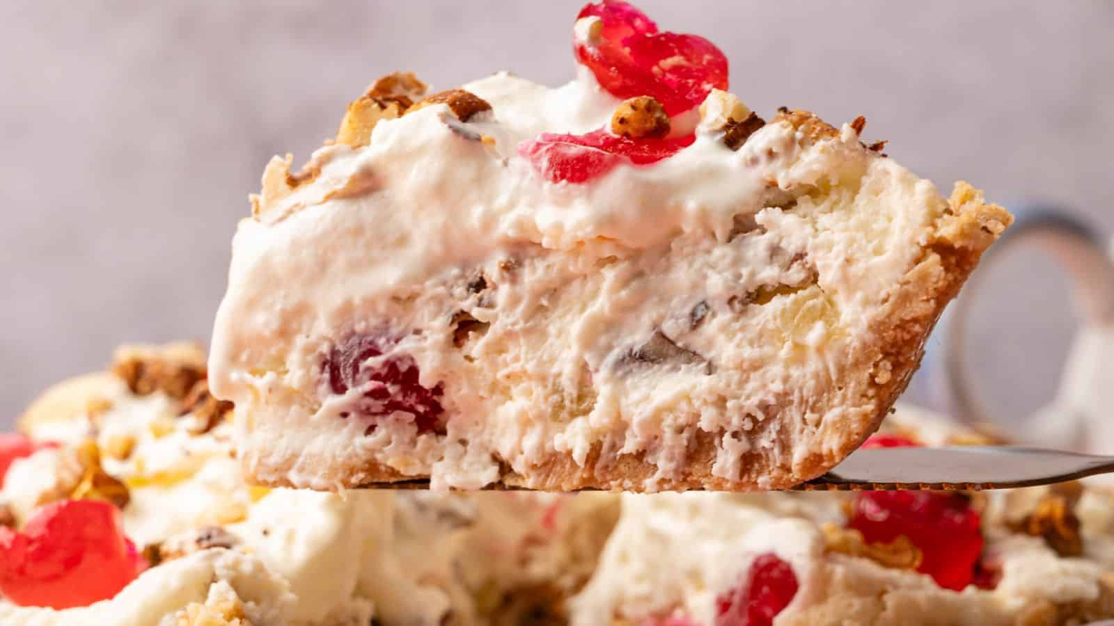 A close-up of a slice of creamy pie with visible cherries, nuts, and a flaky crust, being lifted from the rest of the pie.