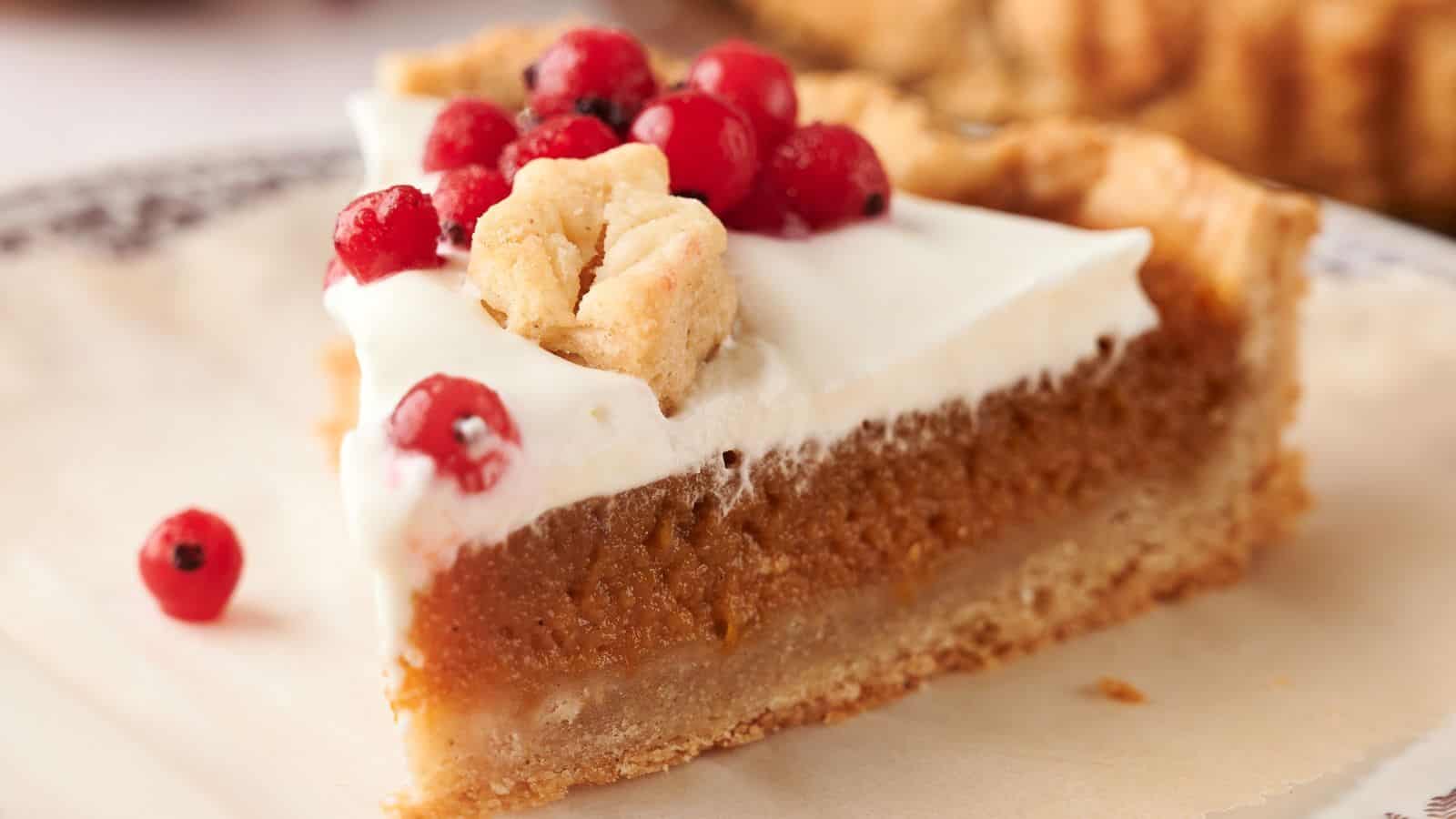 A slice of pie with a creamy white topping, garnished with small red berries and a piece of crumbly crust, on a plate.