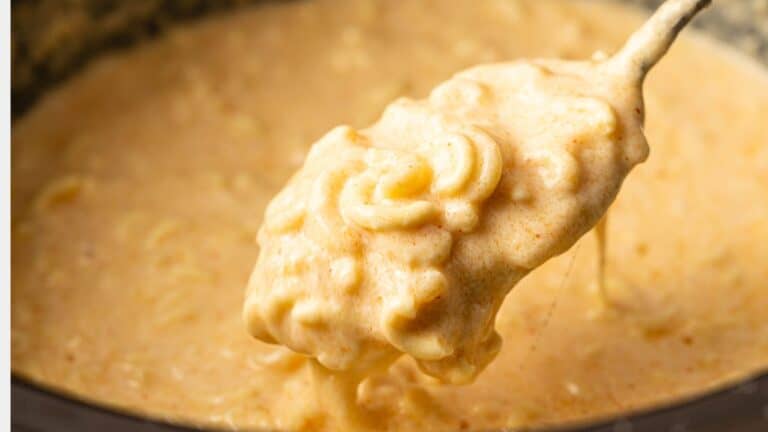 A close-up of a spoon lifting creamy, cheesy macaroni and cheese from a pot.