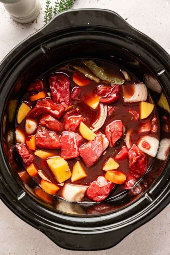 Chunks of raw beef, potatoes, carrots, onions, bay leaf, and broth in a slow cooker—everything you need for a hearty Slow Cooker Beef Stew.