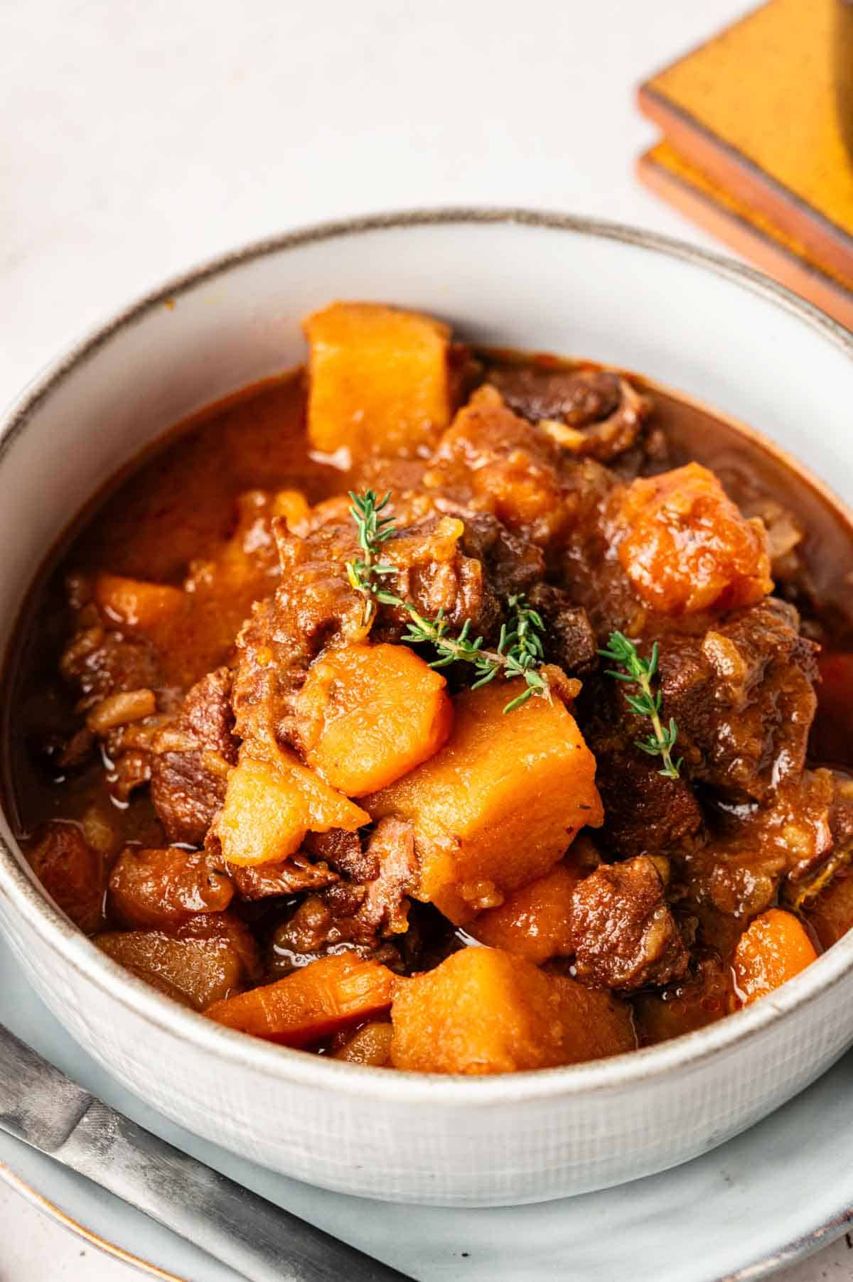 A bowl of Slow Cooker Beef Stew with tender chunks of beef, potatoes, carrots, and a sprig of thyme in a rich, brown broth.