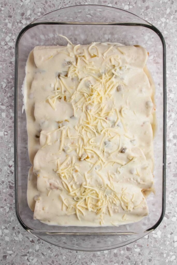 A glass baking dish filled with White Chicken Enchiladas&mdash;rolled tortillas covered in a creamy white sauce and shredded cheese, ready to be baked.