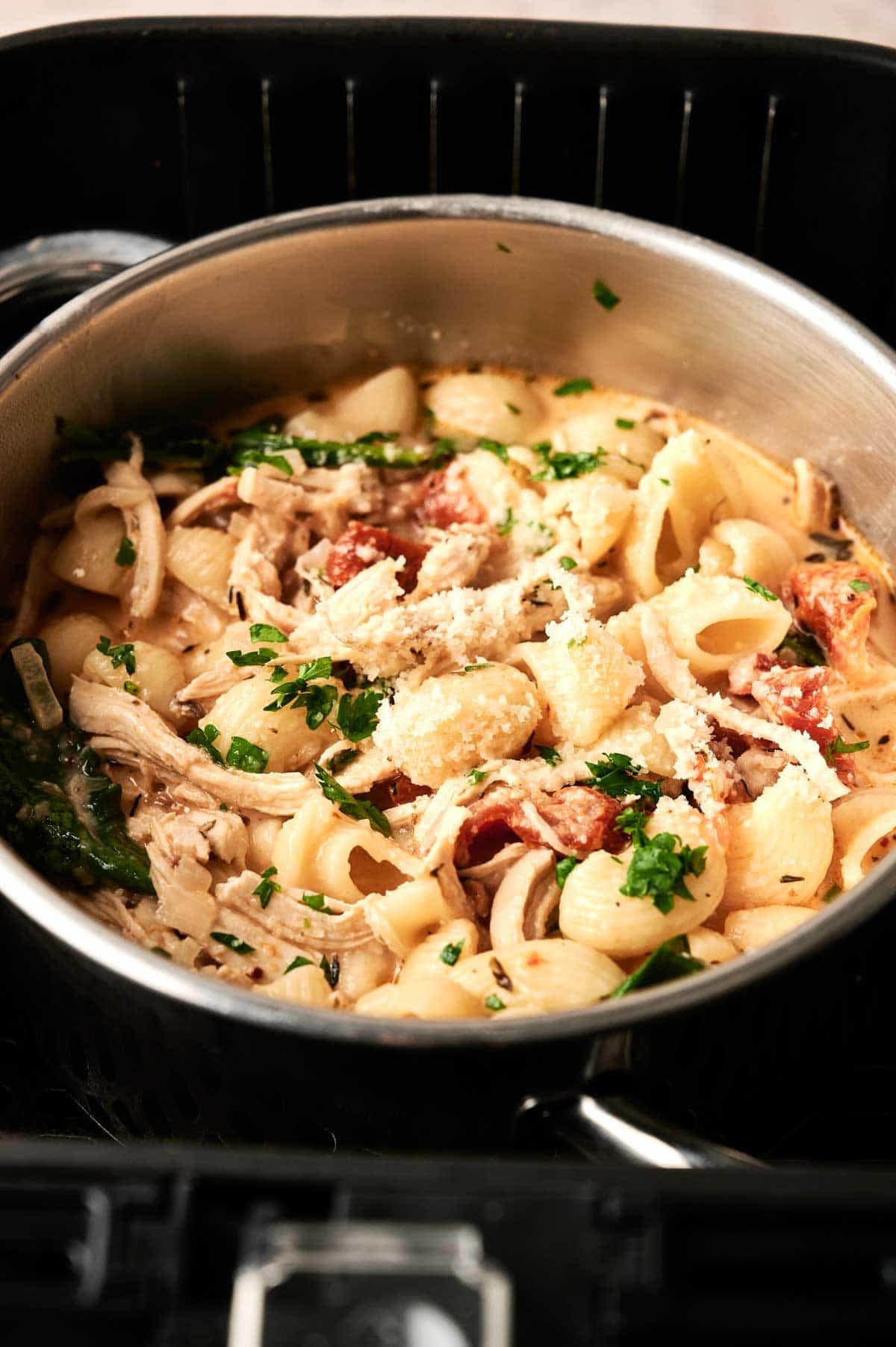 A pot of creamy pasta with shell noodles, shredded chicken, sun-dried tomatoes, grated cheese, and chopped parsley on top&mdash;just like the flavors of Air Fryer Marry Me Chicken Soup in a hearty pasta dish.