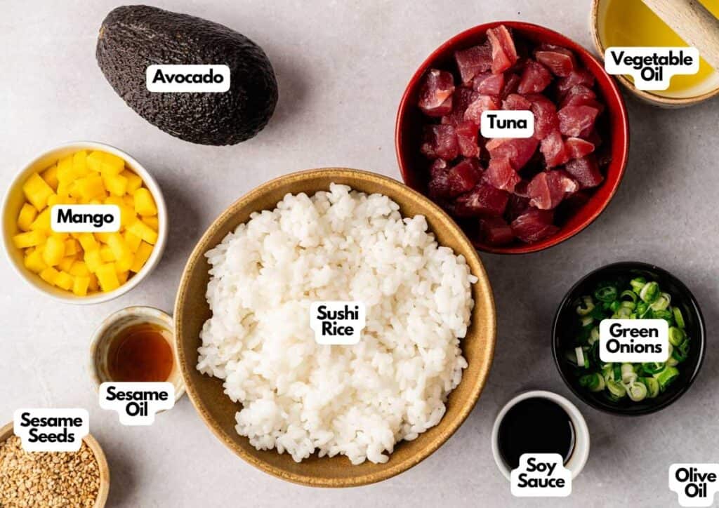 A top-down view of Spicy Tuna Crispy Rice bowl ingredients: avocado, diced tuna, cubed mango, sushi rice, sliced green onions, sesame seeds, sesame oil, vegetable oil, soy sauce, and olive oil.