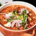 A bowl of Air Fryer Turkey Chili topped with sliced red onions, avocado, sour cream, and chopped cilantro.
