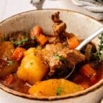 A bowl of Irish Stew with tender beef, potatoes, carrots, and fresh garnish, as a spoon lifts a hearty piece of meat.