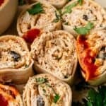 Close-up of Mexican Pinwheels sliced to reveal a creamy mixture, herbs, and chopped vegetables inside; some are topped with tomato sauce and garnished with fresh cilantro.