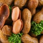 Close-up of Stove Top Boiled Peanuts, with one shell open to reveal two peanuts inside, garnished with parsley.