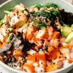 Enjoy a California Roll Sushi Bowl—rice topped with diced imitation crab, avocado, carrots, seaweed, seaweed salad, black sesame seeds, and a creamy orange sauce.