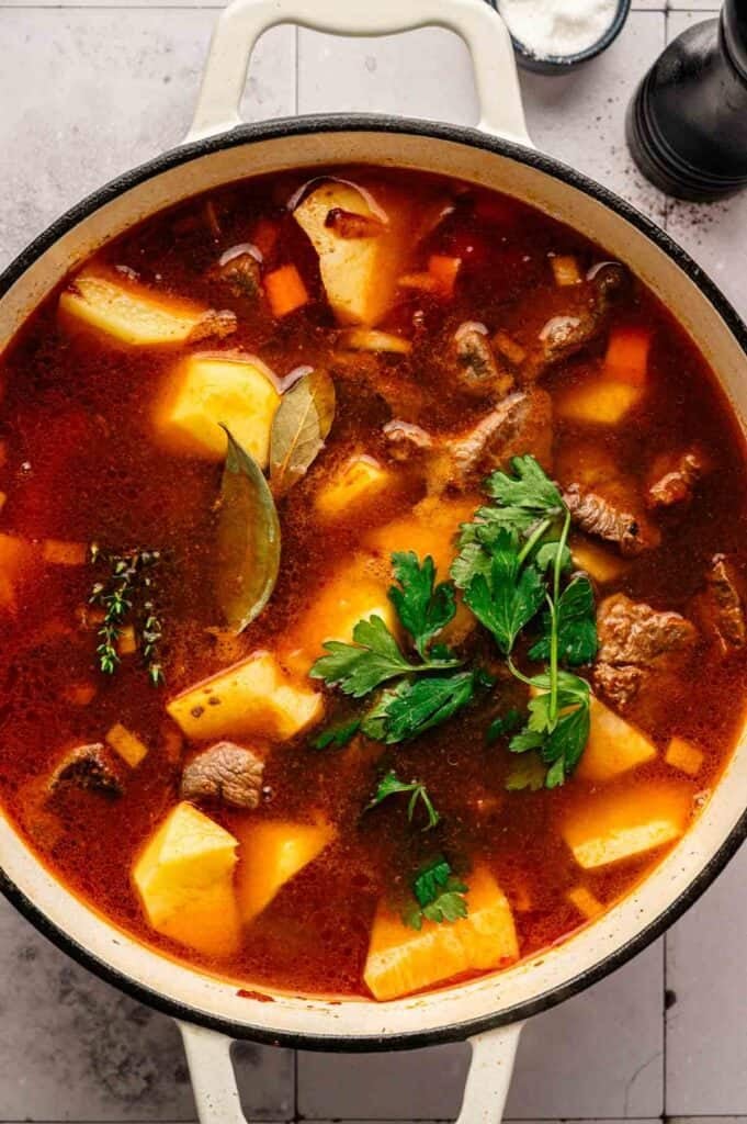 A pot of Irish Stew with tender beef, potatoes, carrots, bay leaves, herbs, and a rich broth, garnished with fresh parsley.