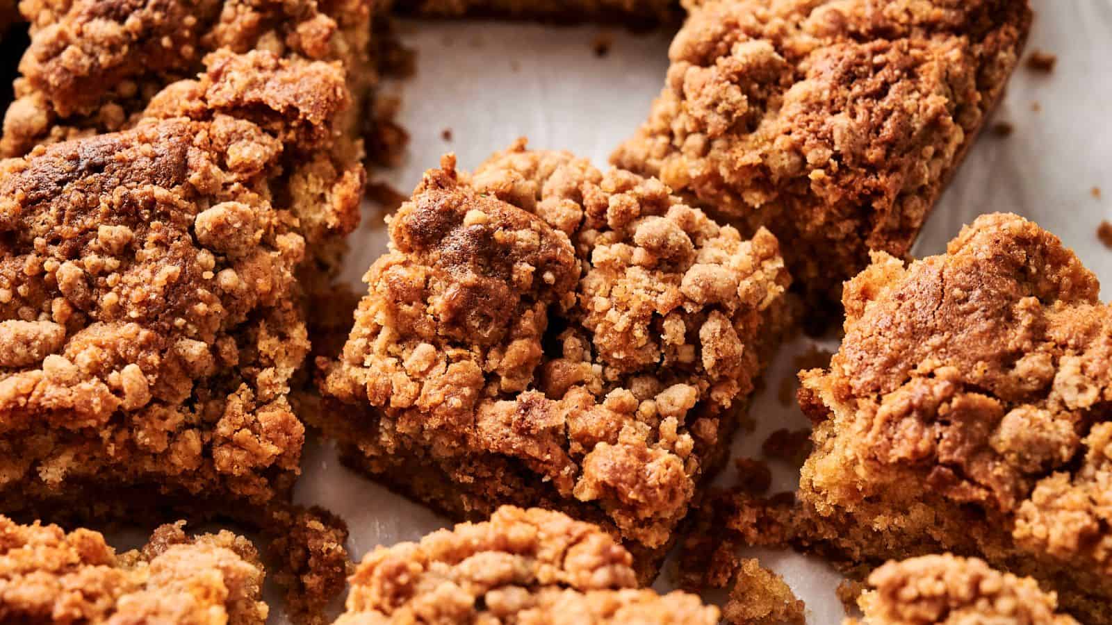 Close-up of several pieces of crumb-topped coffee cake, showing a golden-brown, crumbly texture on a white surface.