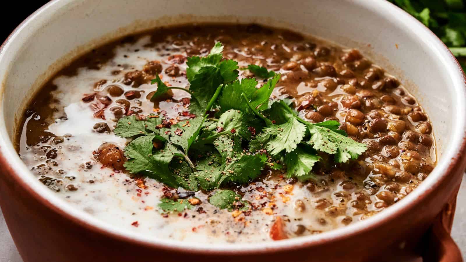 A bowl of lentil soup garnished with fresh cilantro, ground pepper, and a swirl of cream.