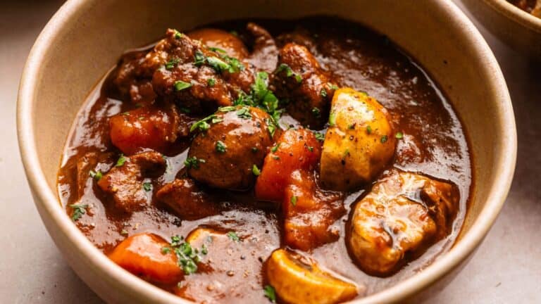 A bowl of beef stew with chunks of beef, carrots, potatoes, mushrooms, and parsley in a thick brown gravy.