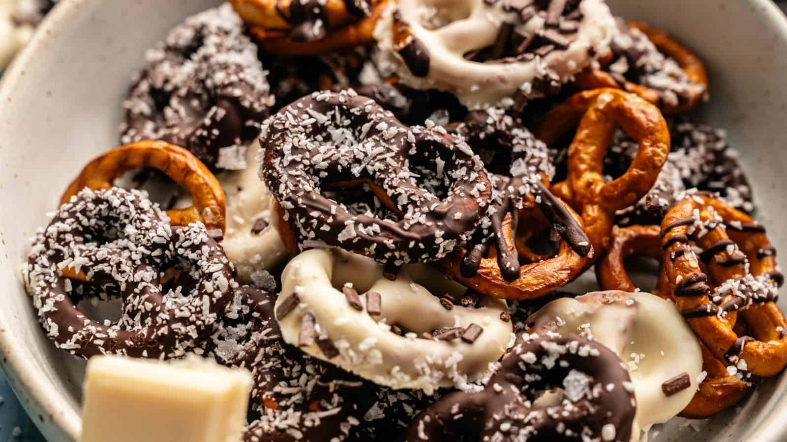 A bowl of pretzels coated in dark and white chocolate, topped with shredded coconut and chocolate sprinkles.