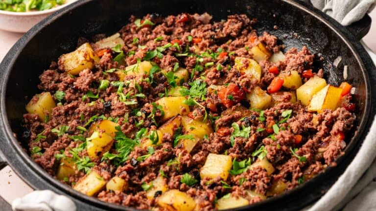 A skillet filled with cooked ground beef, diced potatoes, chopped red peppers, and garnished with fresh parsley.