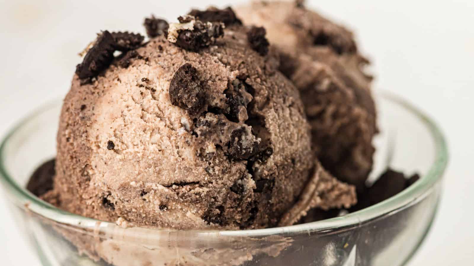 Two scoops of chocolate ice cream with crumbled chocolate cookies on top, served in a clear glass bowl.