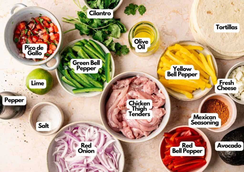 Ingredients for Sheet Pan Fajitas arranged on a countertop: cilantro, olive oil, tortillas, pico de gallo, colorful bell peppers, lime, pepper, salt, chicken thigh tenders, red onion, cheese, seasoning, and creamy avocado.