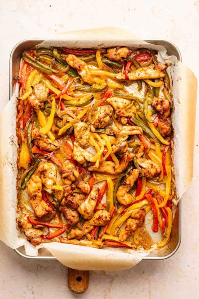 Sheet Pan Fajitas made with baked chicken strips and red, yellow, and green bell peppers on a parchment-lined baking tray.