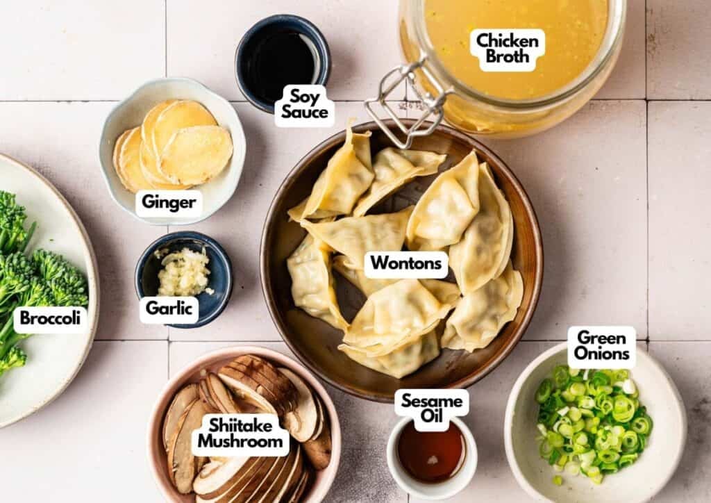 A bowl of Wonton Soup surrounded by labeled ingredients: chicken broth, green onions, sesame oil, shiitake mushrooms, broccoli, garlic, ginger, and soy sauce.