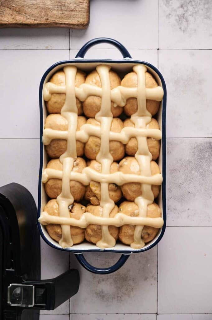 Unbaked hot cross buns arranged in a dish with cross piping
